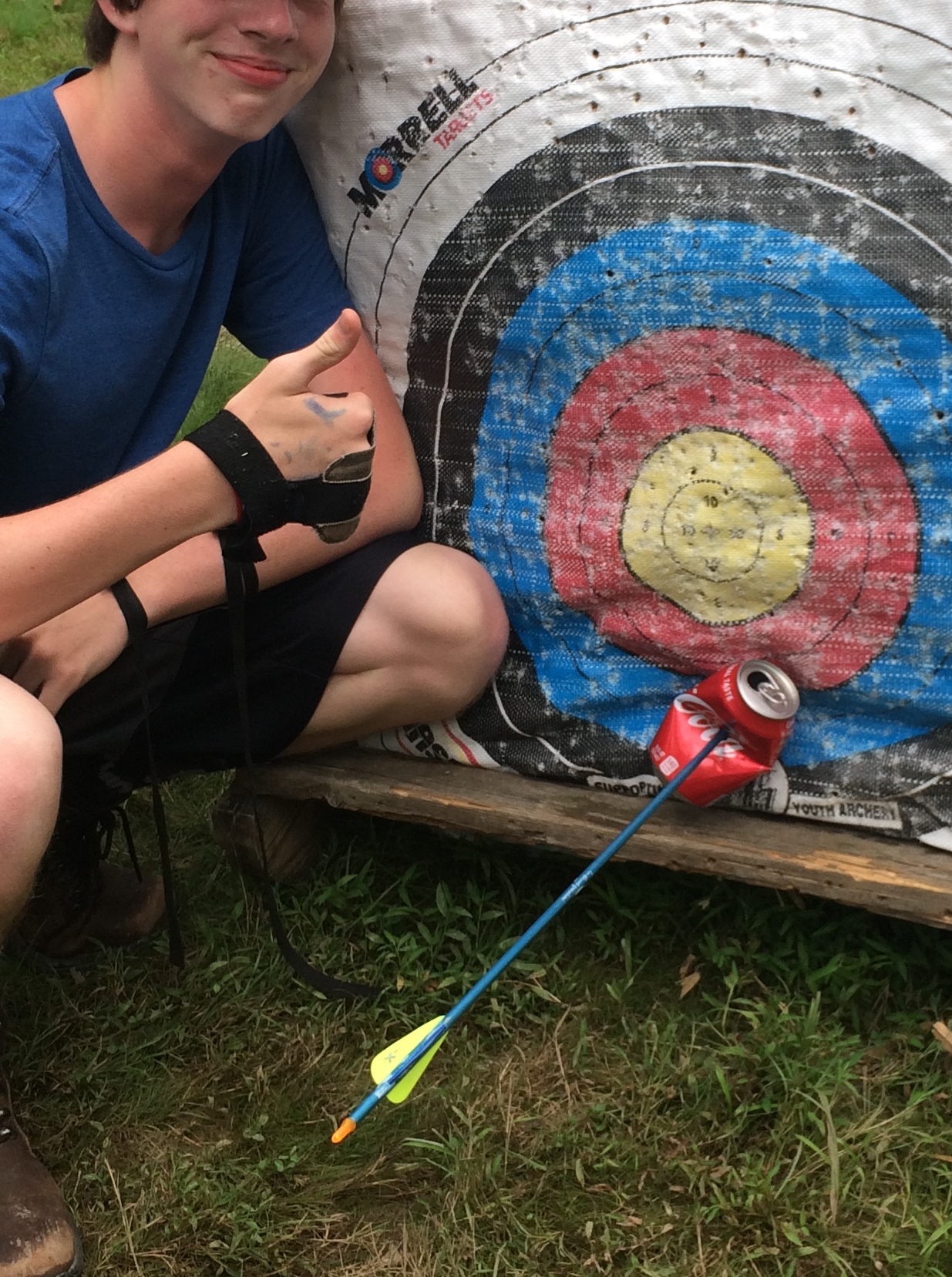 A 17-year-old giving a thumbs up next to a target, where an arrow has pierced his soda can.