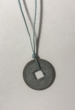 A Feng Shui coin hangs on a sky-blue thread as a pendant.