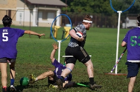 A quidditch player stepping over William as he falls backward in the mud, wearing a keeper's headband.